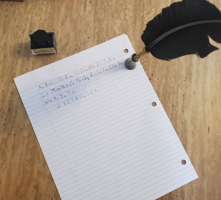 a feather dip pen, an inkwell, and a sheet of lined paper with the alphabet and numbers 0-9 written on it. a feather dip pen, an inkwell, and a sheet of lined paper with the alphabet and numbers 0-9 written on it.